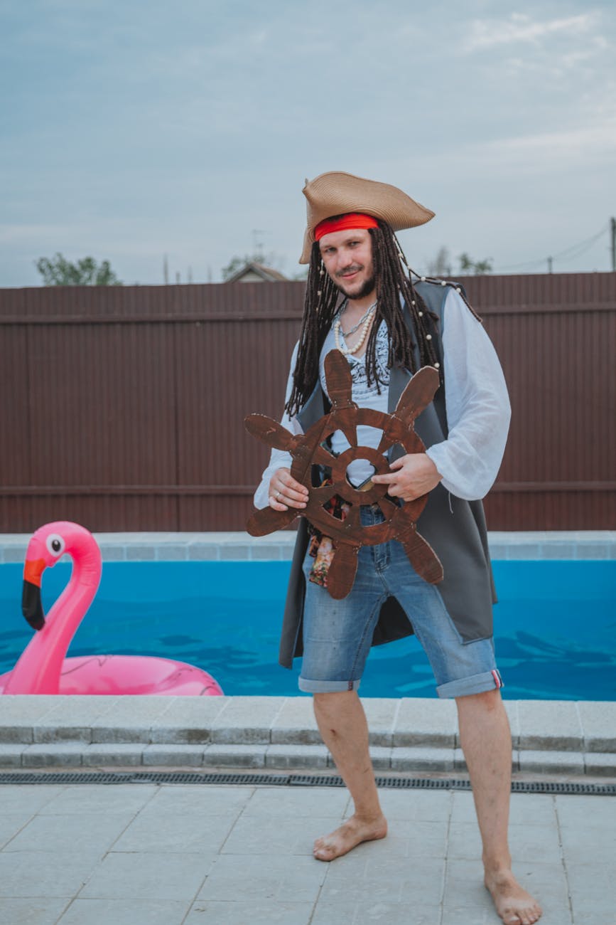 happy young actor in pirate costume standing on poolside with inflatable flamingo mattress